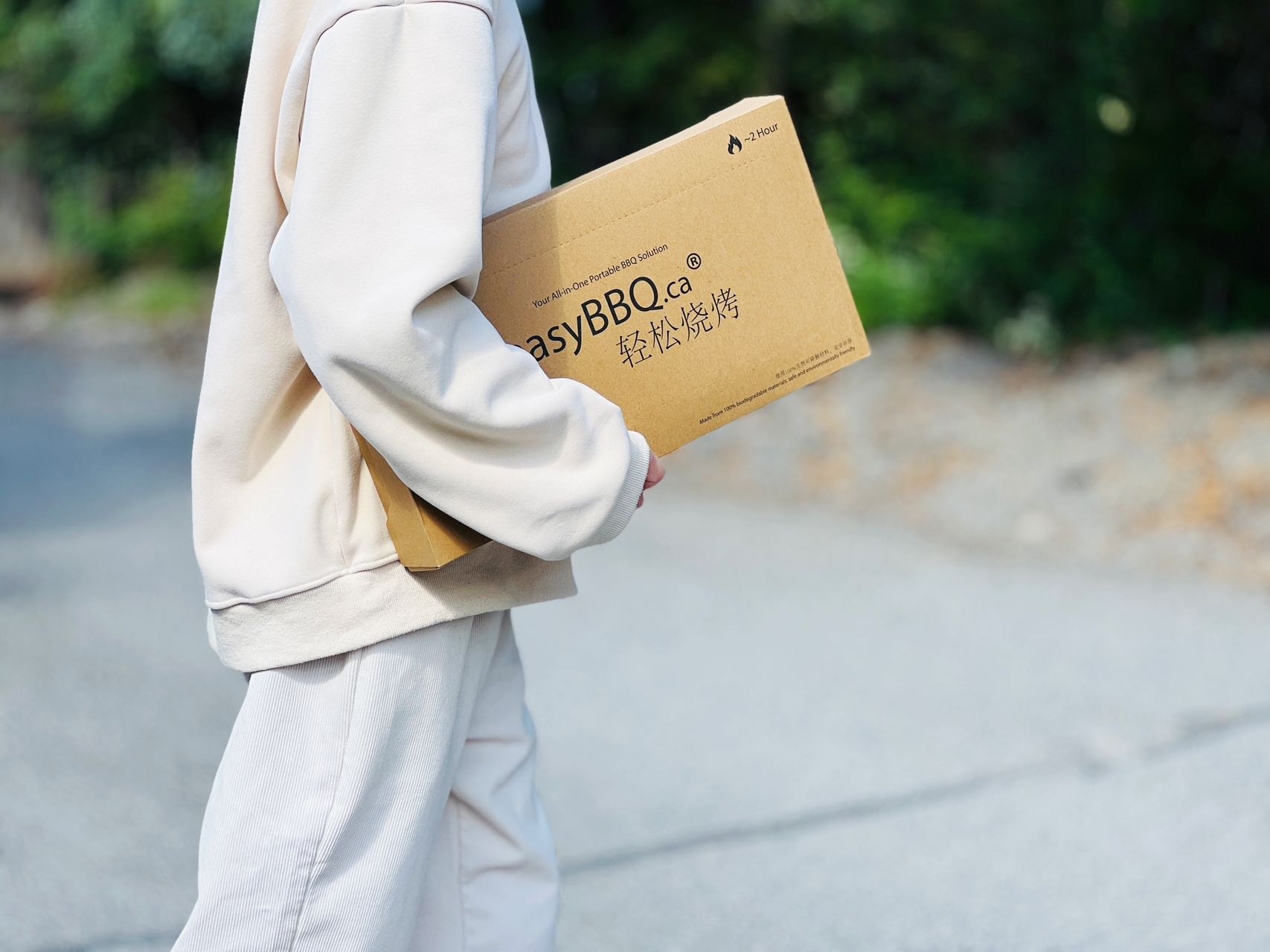 Person carrying a compact EasyBBQ grill box outdoors